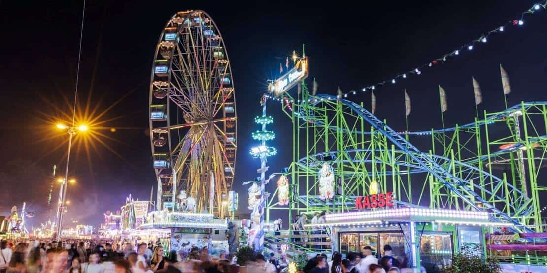 Blick hinter die Kulissen des Hannover Schützenfests mit Riesenrad und Fahrgeschäften bei Nacht.