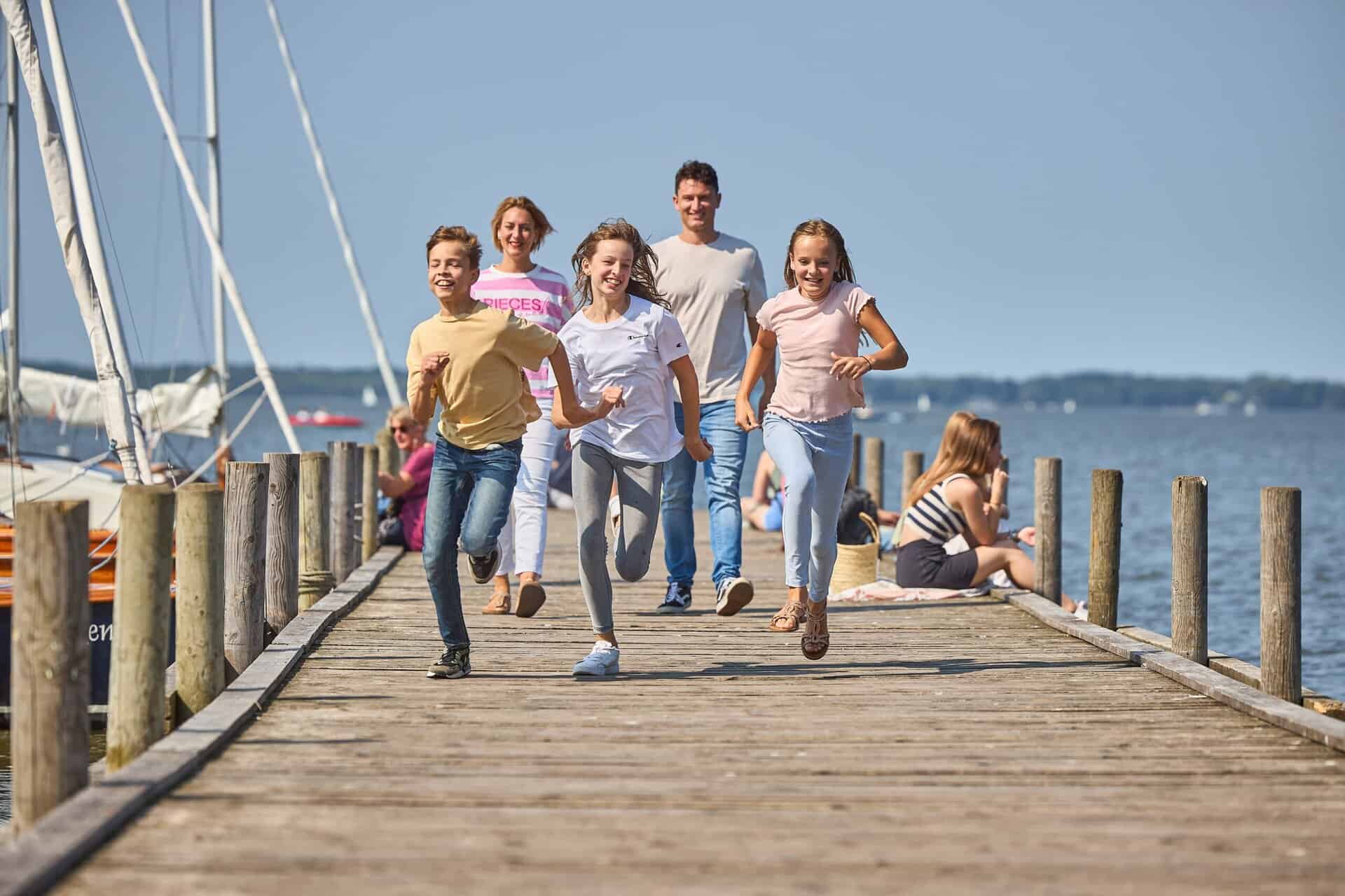 Familie läuft fröhlich auf Steg am Wasser.
