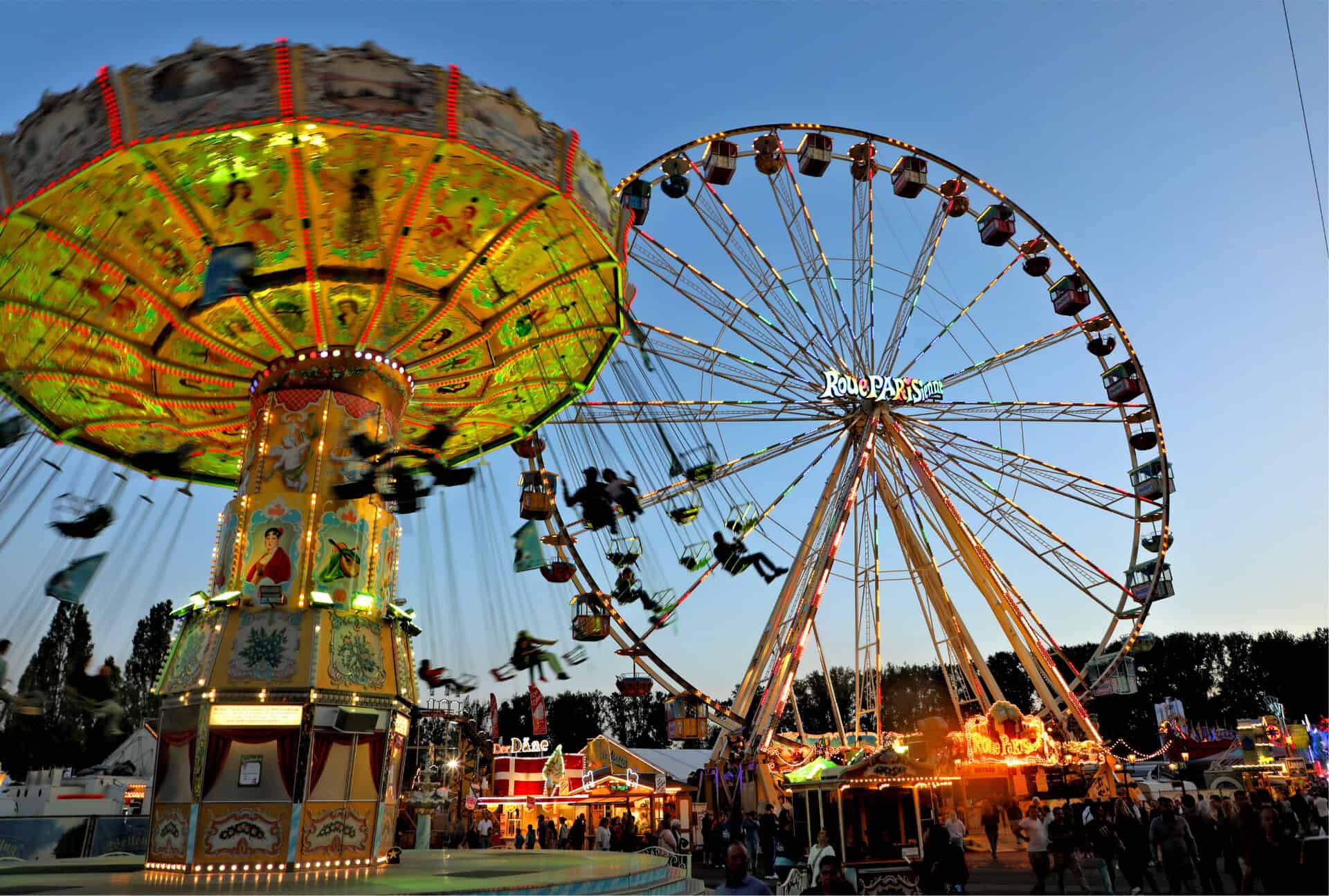 Vue de la grande roue et du carrousel lors de la fête des tireurs de Hanovre 2025 au coucher du soleil.
