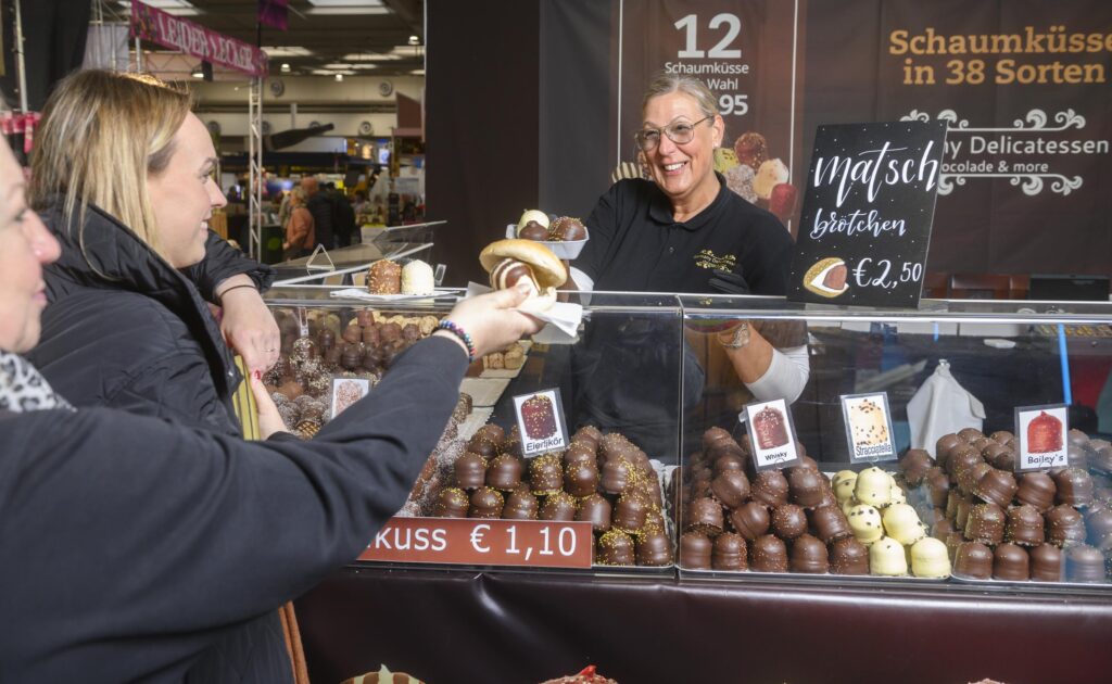 Eine Frau gibt Backwaren an einem Stand auf der Erlebnis- und Einkaufsmesse infa an zwei Gäste.