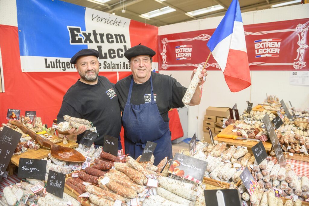 Zu sehen sind 2 Männer an einem Salamistand auf der Erlebnis- und Einkaufsmesse infa.