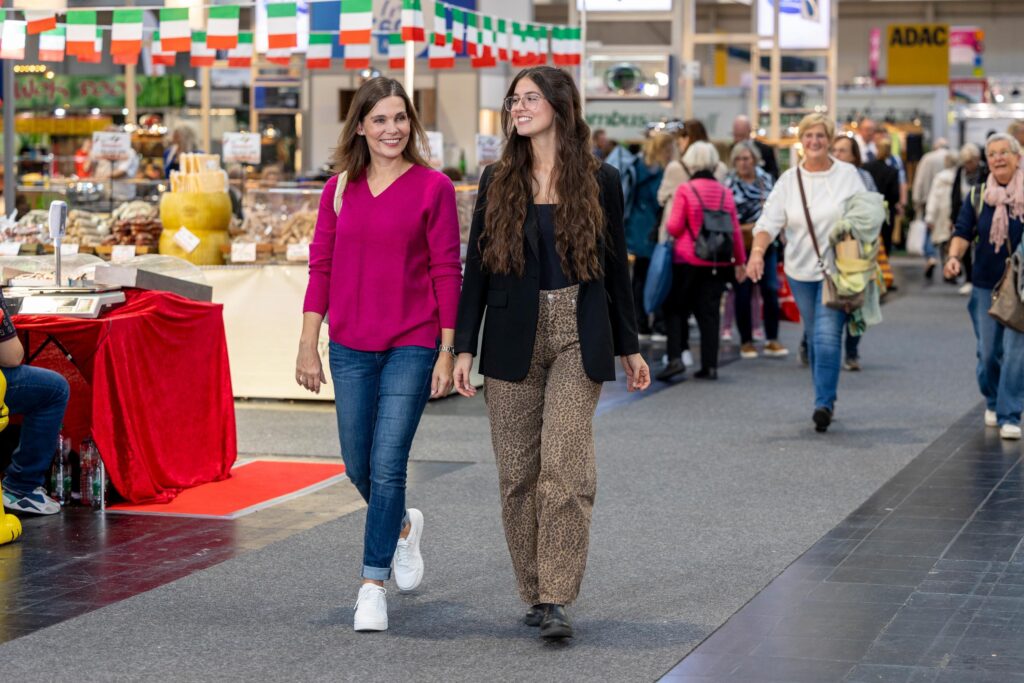 Zu sehen sind zwei Frauen am Schlendern auf der Erlebnis- und Einkaufsmesse infa. Im Hintergrund sind Stände und andere Gäste.