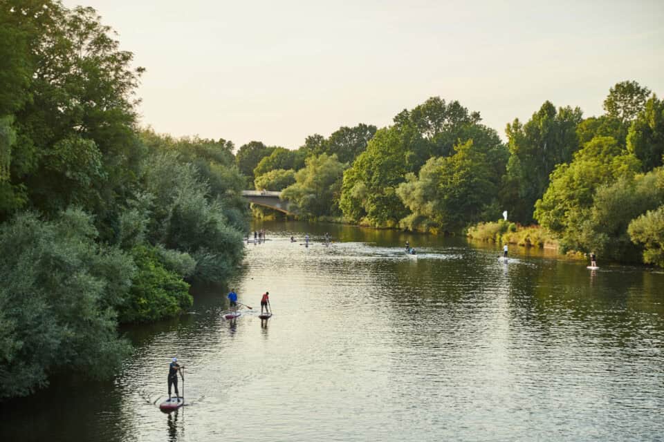 Menschen beim Stand up Paddling auf ruhigem Fluss in Hannover, umgeben von Natur.