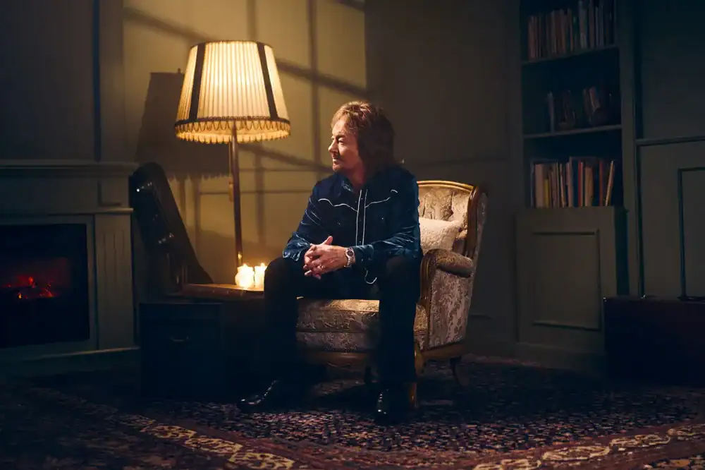 Chris Norman zit ontspannen in een gezellige ruimte met warm licht.