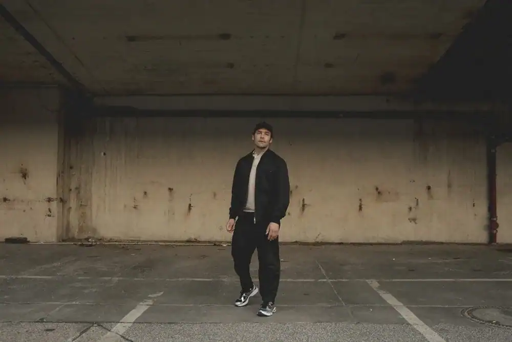 Bosse stands in front of a grey wall in an empty, underground car park.