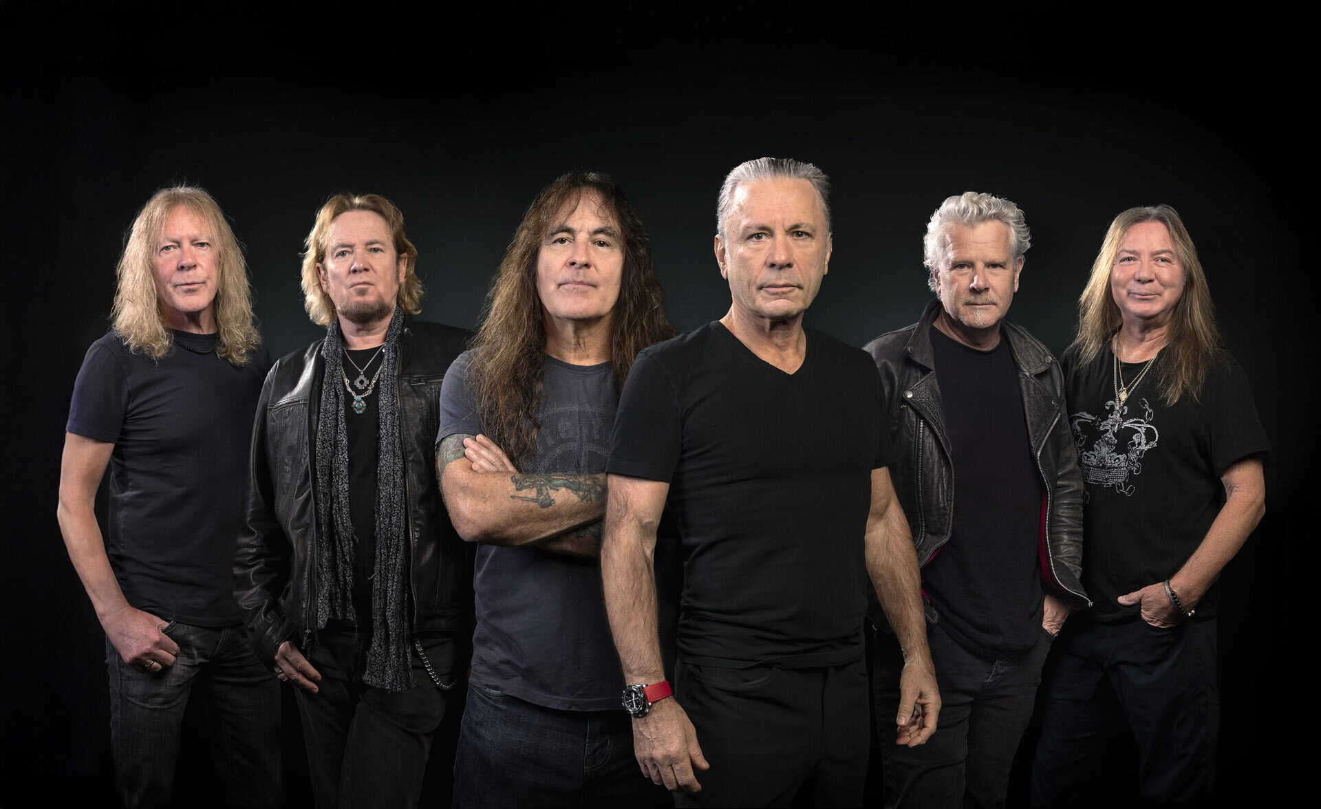 Легендарная хэви-метал группа Iron Maiden на концерте, все участники на фоне темного фона.