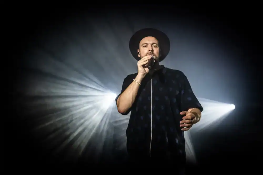 Max Mutzke canta no palco com holofotes ao fundo.