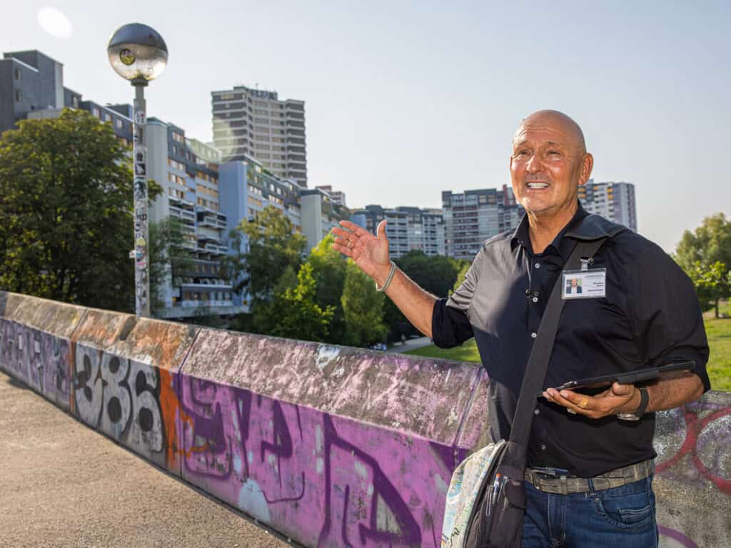 Stadtführer in Hannover zeigt Graffiti-Kunst an einer Brücke mit modernen Gebäuden im Hintergrund.