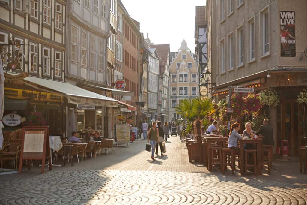 Altstadt Hannover mit Straßencafés und Fußgängern, sonniges Wetter, lebendige Atmosphäre.