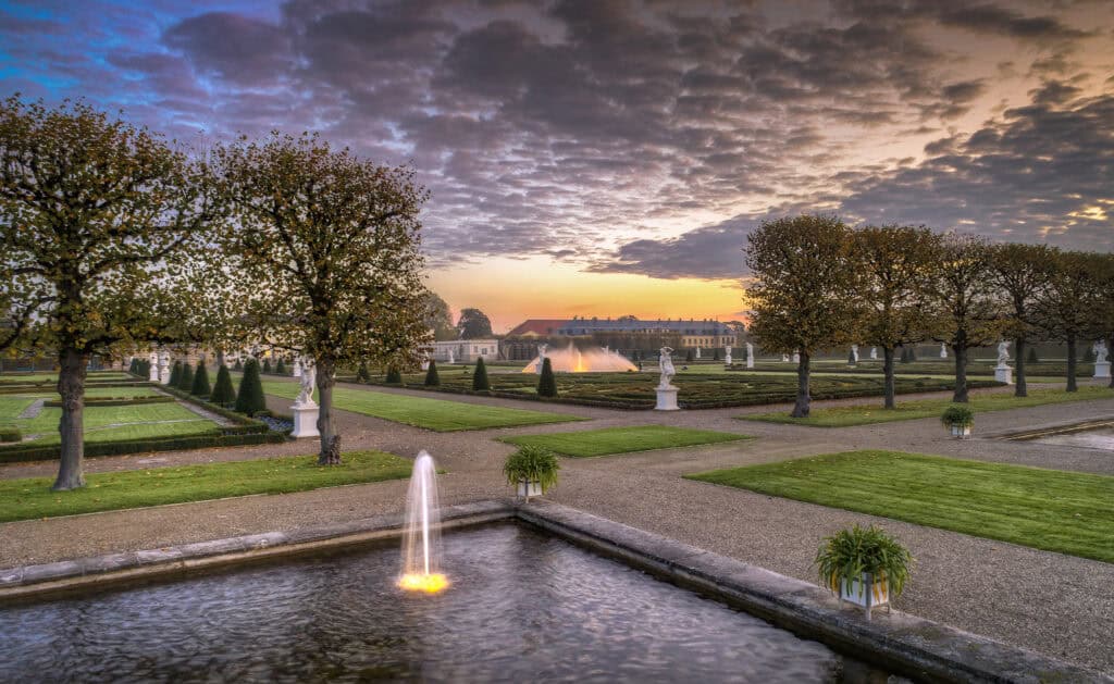 Barockgarten Hannover mit Springbrunnen und gepflegten Wegen bei Sonnenuntergang.