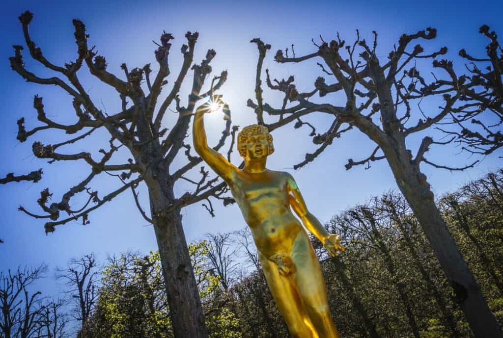 Skulptur von Geheimrat Leibniz im Barockgarten mit blühenden Bäumen im Hintergrund.