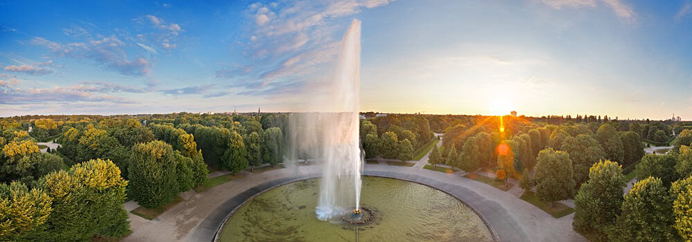 Blick auf die Herrenhäuser Gärten mit Springbrunnen bei Sonnenuntergang in Hannover.