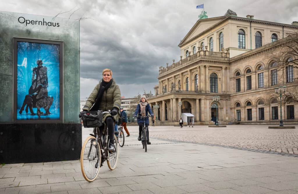 Fahrradfahrer erkunden Hannover bei der Krimitour, vorbei am Opernhaus und historischen Gebäuden.