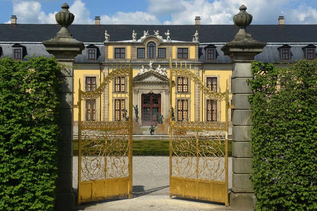 Barockgarten mit goldenen Toren und prächtigem Schloss im Hintergrund.