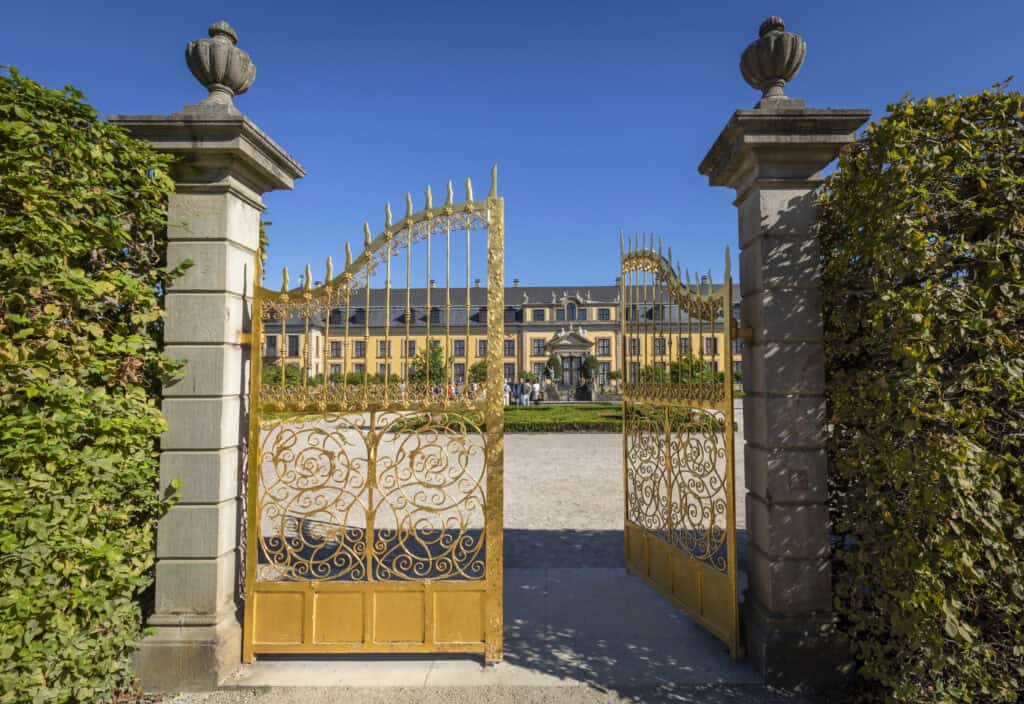 Blick auf den Herrenhäuser Garten mit goldener Pforte und barockem Schloss im Hintergrund.