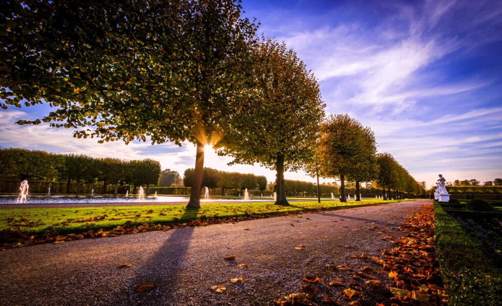 Herrlicher Blick auf den Herrenhäuser Garten bei Sonnenuntergang, mit Bäumen und Wasserfontänen.