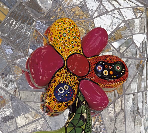 Farbige Skulptur einer Blume von Niki de Saint Phalle im Spiegelglas-Umfeld.