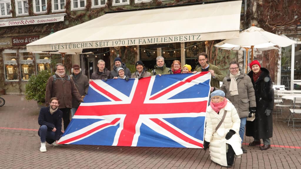 En gruppe mennesker holder et stort britisk flag uden for en café i Hannover.