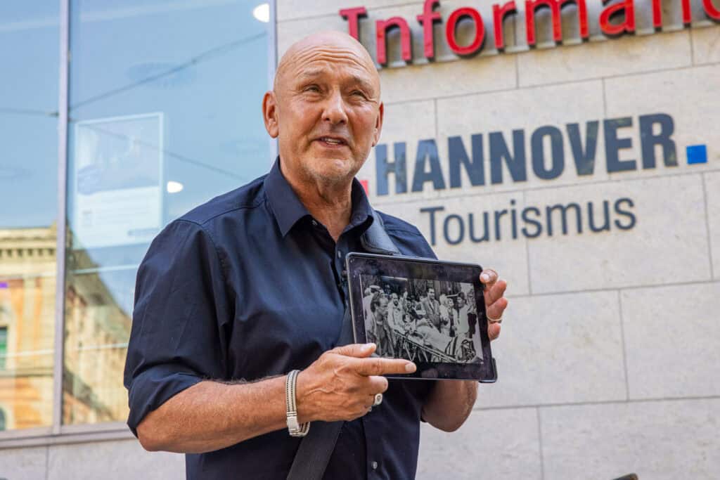 Mann zeigt historische Fotos vor dem Hannover Tourismus-Informationszentrum.
