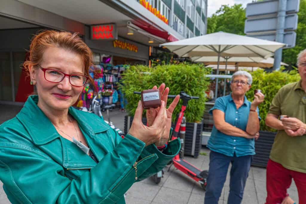 Frau zeigt Nascherei vor einem Geschäft in Hannover, mit Freunden im Hintergrund.