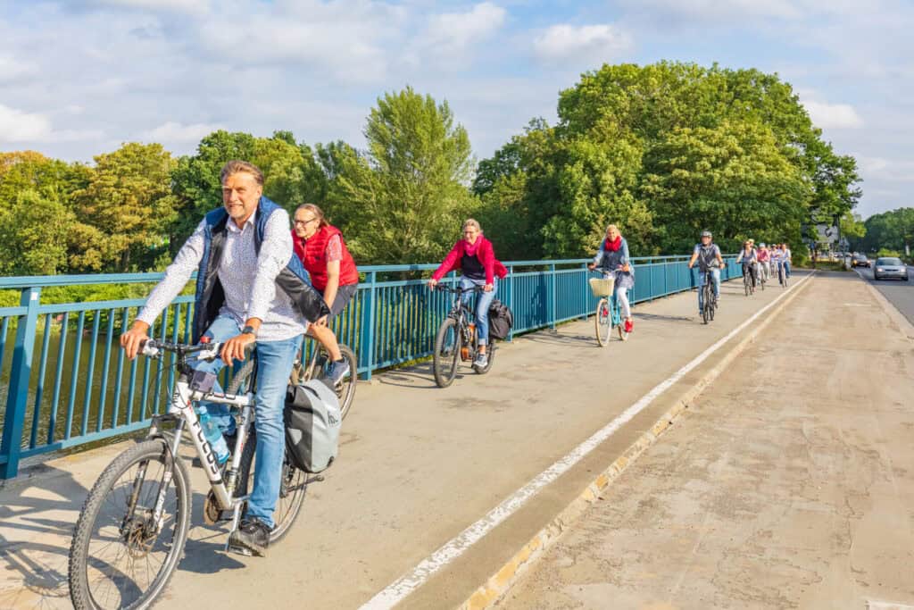 Gruppe von Radfahrern auf der Fahrradbrücke in Hannover, umgeben von Bäumen.