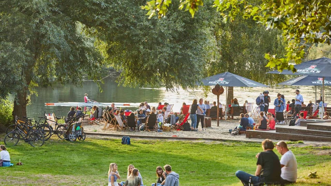 Хора се наслаждават на слънцето и природата край езерото Машзее в Хановер, с лодки и пикници в парка.