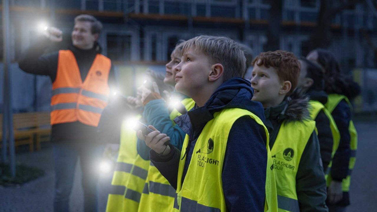 Children with high-visibility waistcoats and torches on a construction site tour.