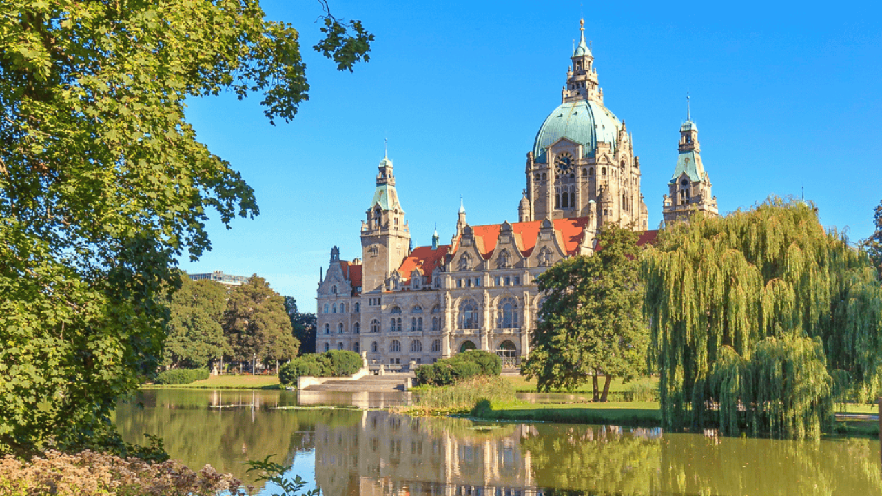 Vista del ayuntamiento histórico en el centro de Hannover, rodeado de naturaleza.