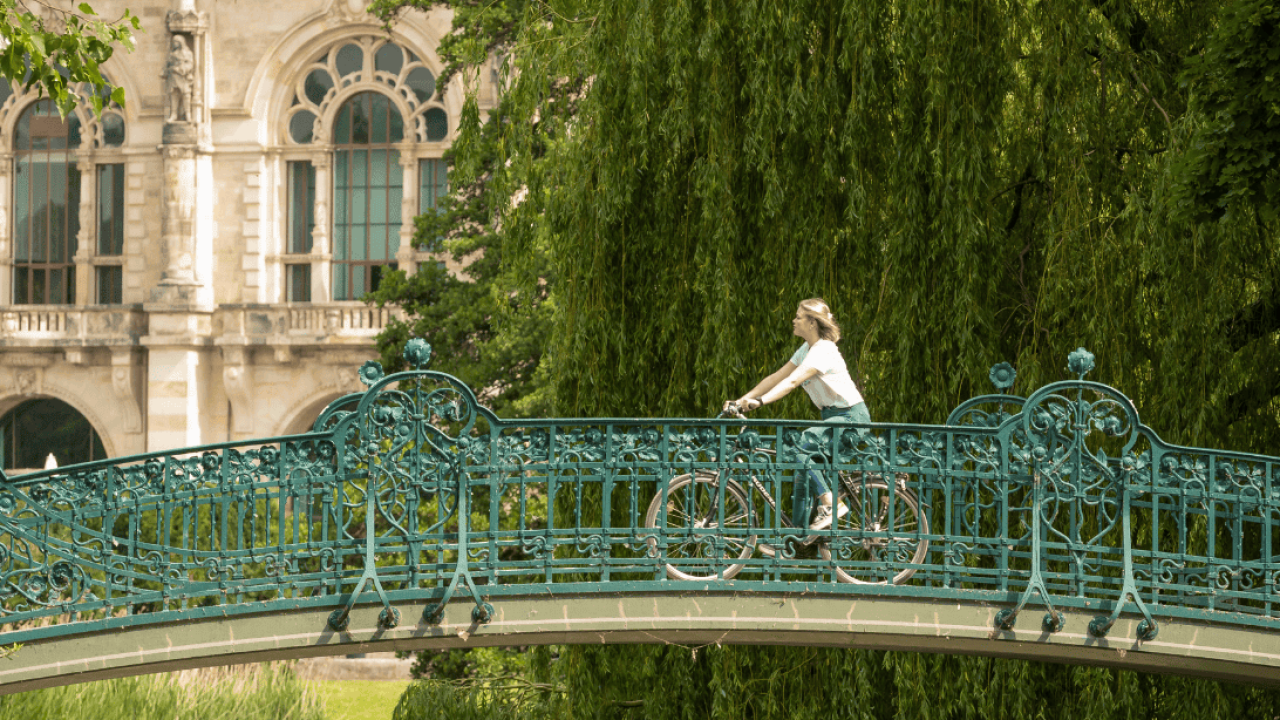 Ponte em Hanôver com ciclista, rodeada por árvores verdes e um edifício histórico ao fundo.