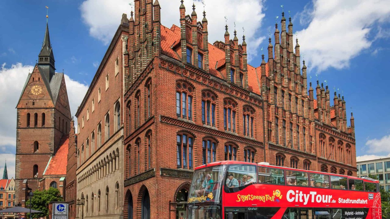 Edificio storico di Hannover con autobus turistico rosso in primo piano.