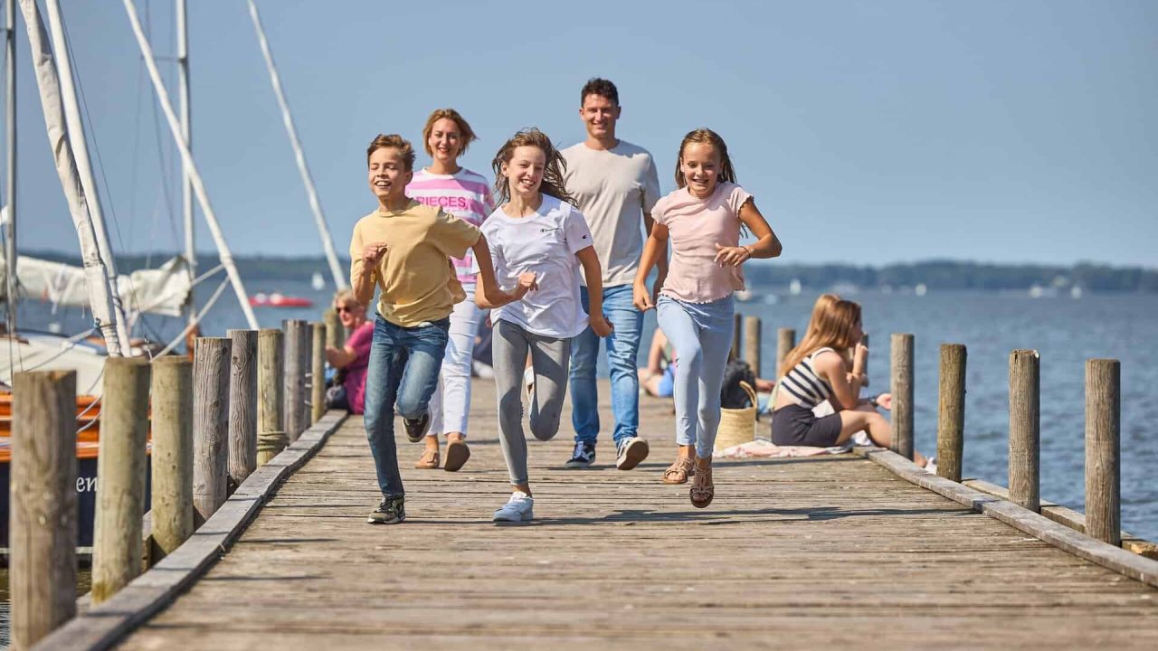 Familie läuft fröhlich auf Steg am Wasser.
