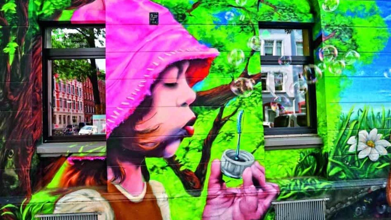 花と木が描かれた落書き壁に絵を描くピンクの帽子をかぶった少女。.